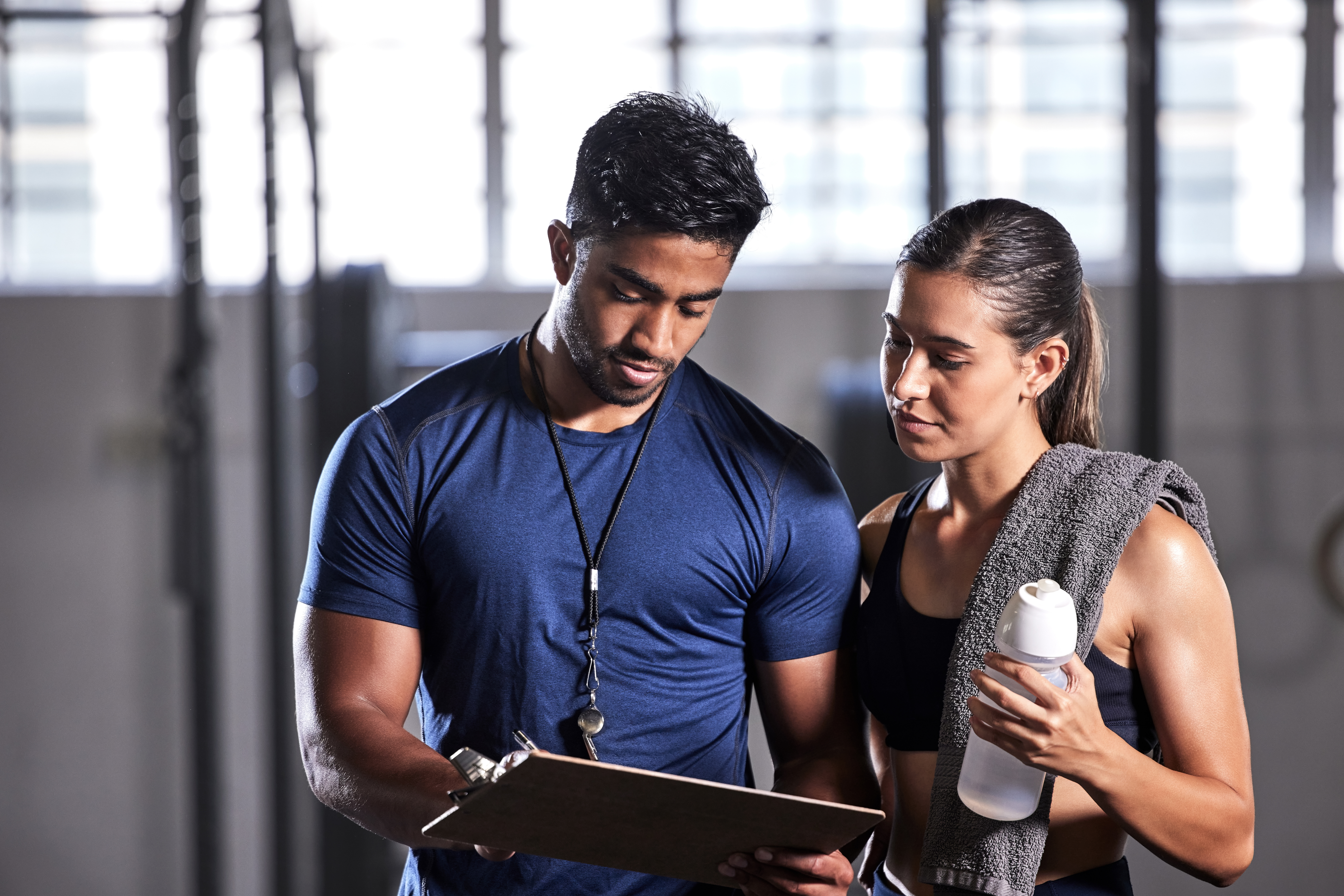 Coach planning workout, schedule and training with athlete for active, fitness and wellness in a gym. Trainer writing notes for sports client with routine to gain toned, strong and fit body muscle
